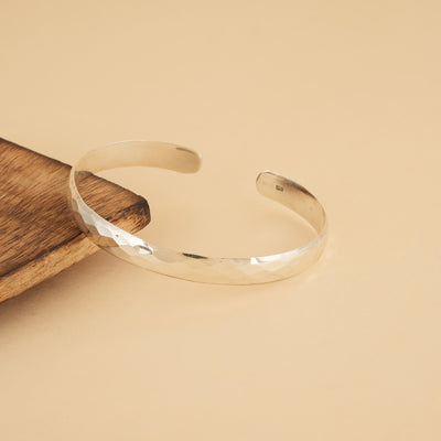 Silver open bracelet on a wooden surface with a beige background