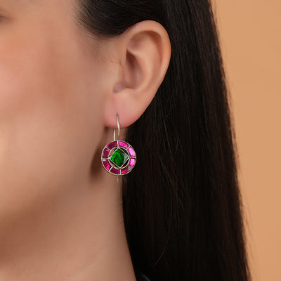 Close-up of a silver earring with a green and pink kundan work on a model against a beige background