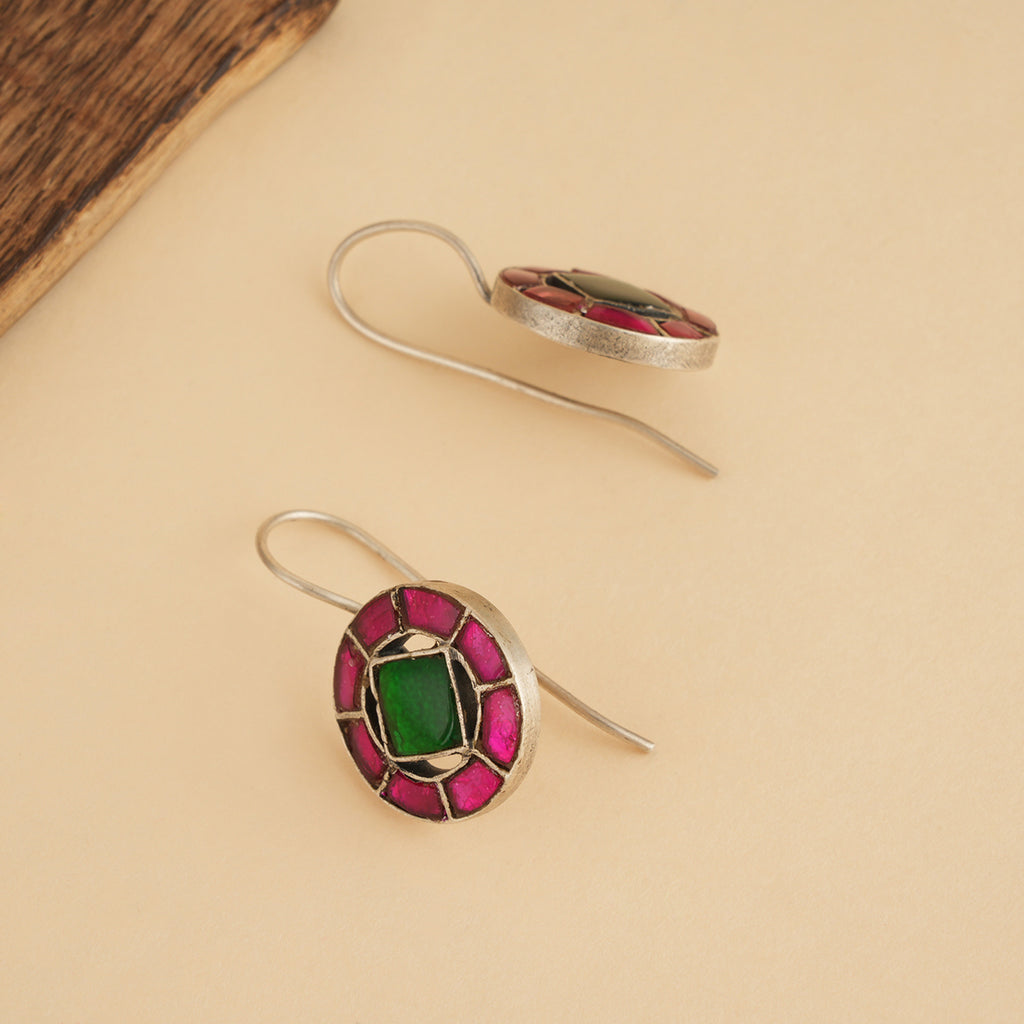 Silver kundan work earrings with green and pink stones on a beige surface