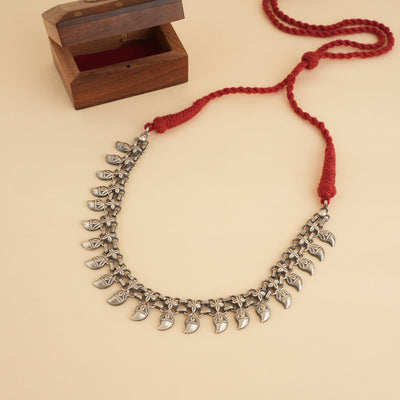 Silver choker necklace in paisley design with red thread on a beige background