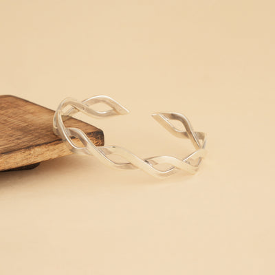 Silver open kada bracelet on a wooden block with a beige background